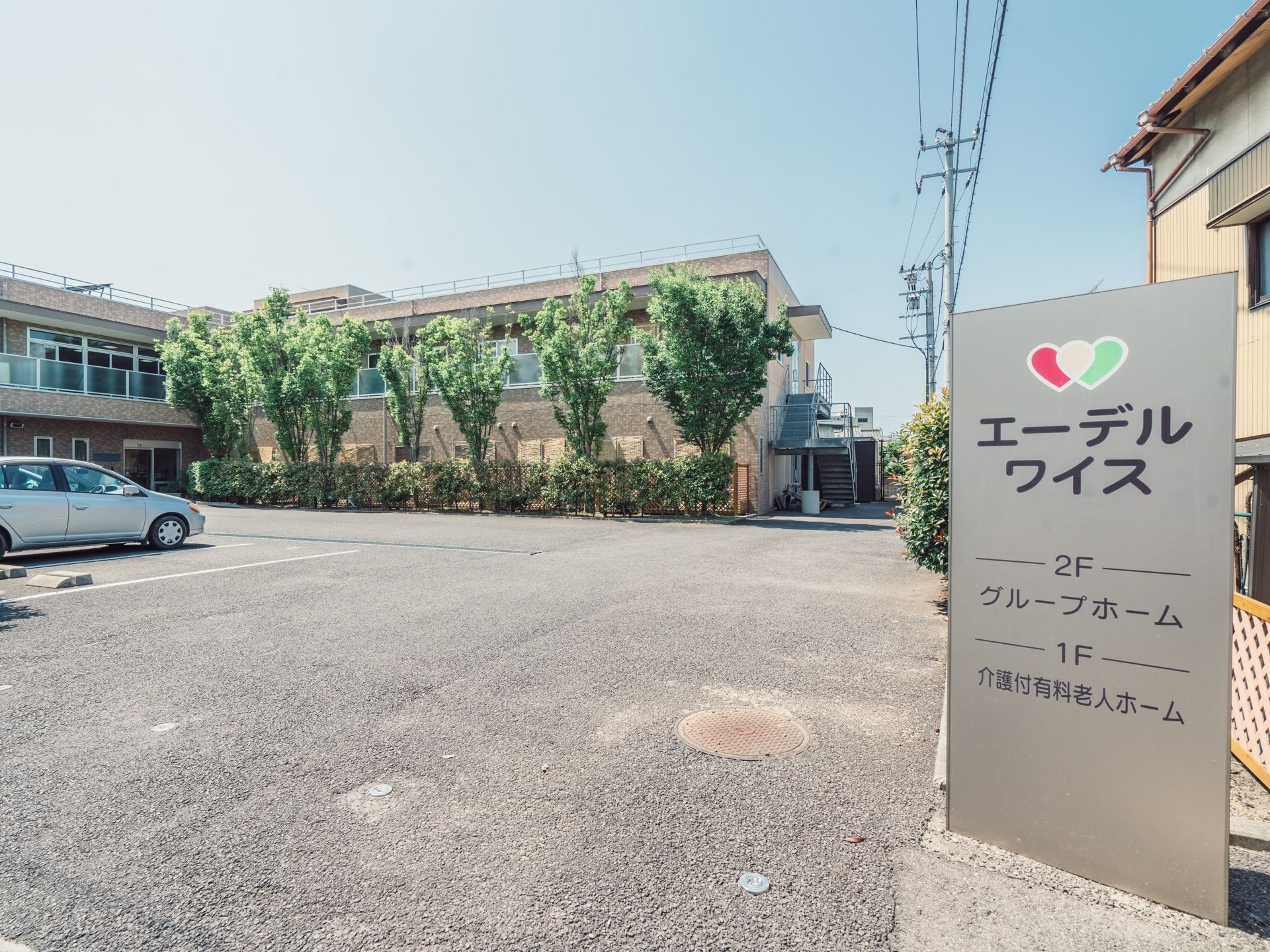 ２階建ての施設があり、建物の前に同じくらいの高さの木が並んで茂っている。舗装された広い駐車場を完備している。