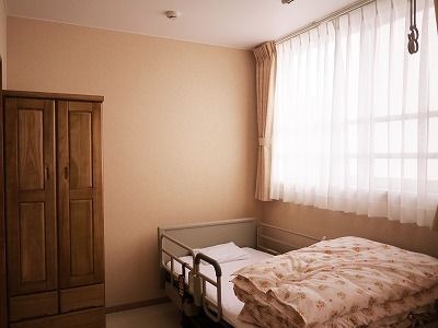 花柄の寝具がセットされた介護ベッドのそばには大きな窓があり、木製のクローゼットも置かれている。