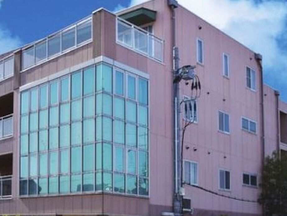日当たりのいい場所に建っているブラウン系の建物は大きく、一面がガラス張り。周りには草木が植えられている。
