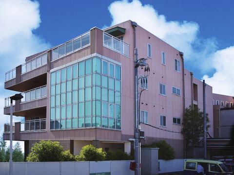 屋外で笑顔で過ごしている車いすの高齢女性と付き添いのエプロンを付けた若い男性スタッフ。