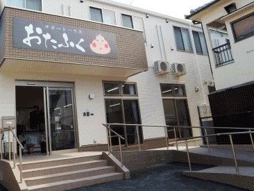 おたふくのイラストが描かれた外壁が印象的。ベージュやブラウンでまとめられた２階建ての建物。