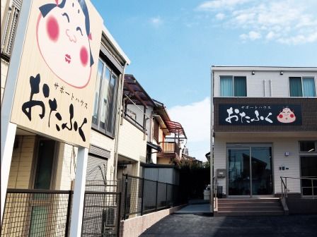 看板が付き敷地内には駐車スペースもある、2階建ての建物の外観にもおたふくの描かれている。