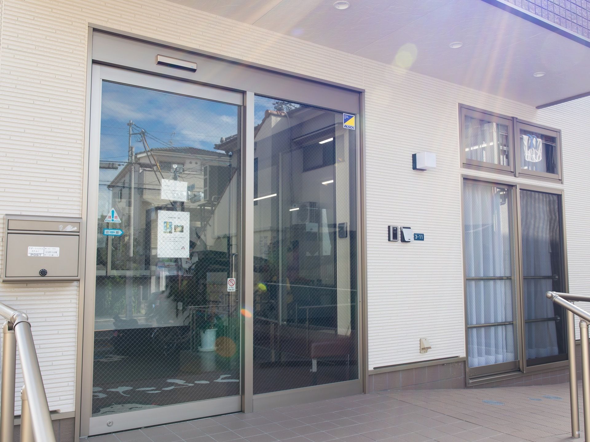 玄関前は、手すり付きの緩やかなスロープになっている。自動ドアがあり、ガラスには飛散防止のワイヤーが入っている。