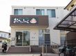 ２階建ての住宅が建っている。玄関前は手すりの付いた階段とスロープが設けられている。手前には屋根付きの駐輪場もある。