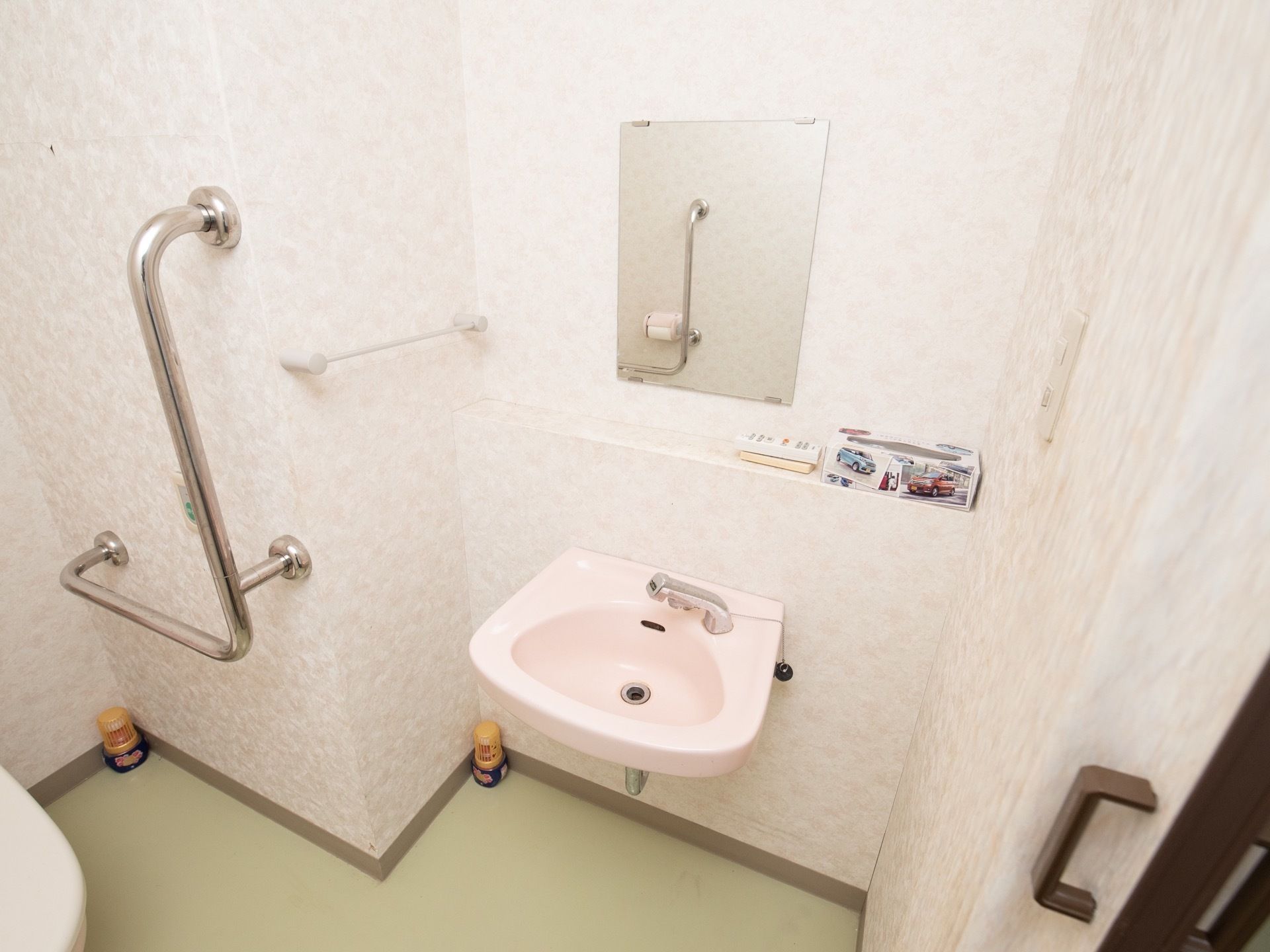 淡いピンクで統一された、落ち着きのあるトイレである。アコーディオンカーテンで開閉可能で、洗面スペース、手すりが完備されている。