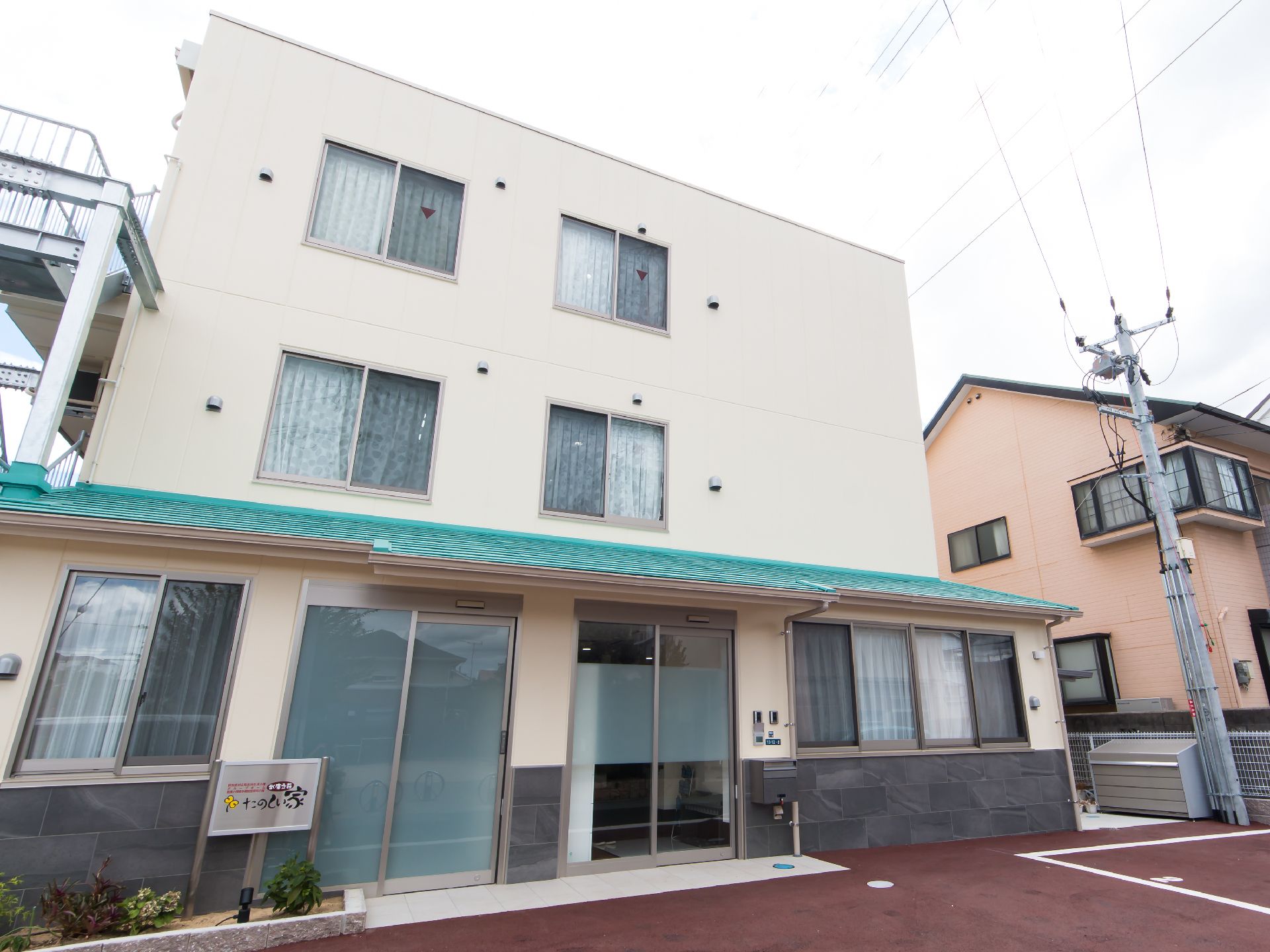 植え込みに施設看板を立て非常階段を備えた３階建ての施設
