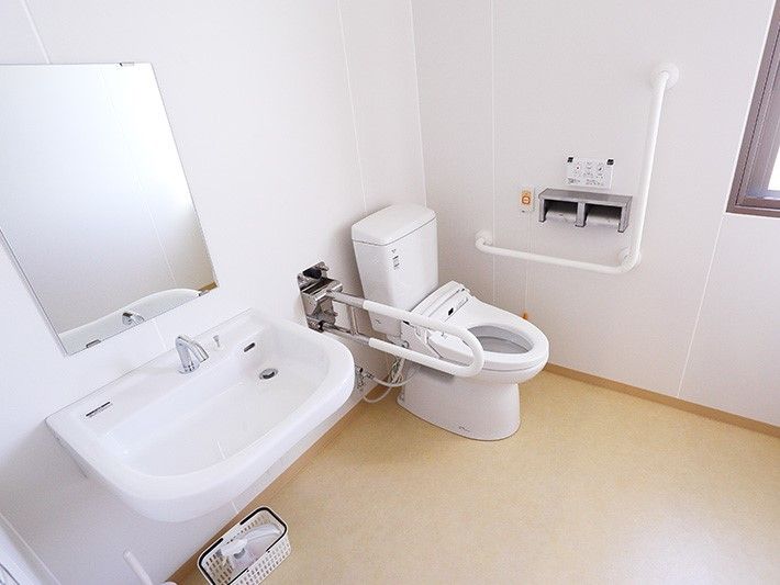 広いトイレには鏡付きの手洗い場もあり、トイレの両サイドに手すりが設置されている。