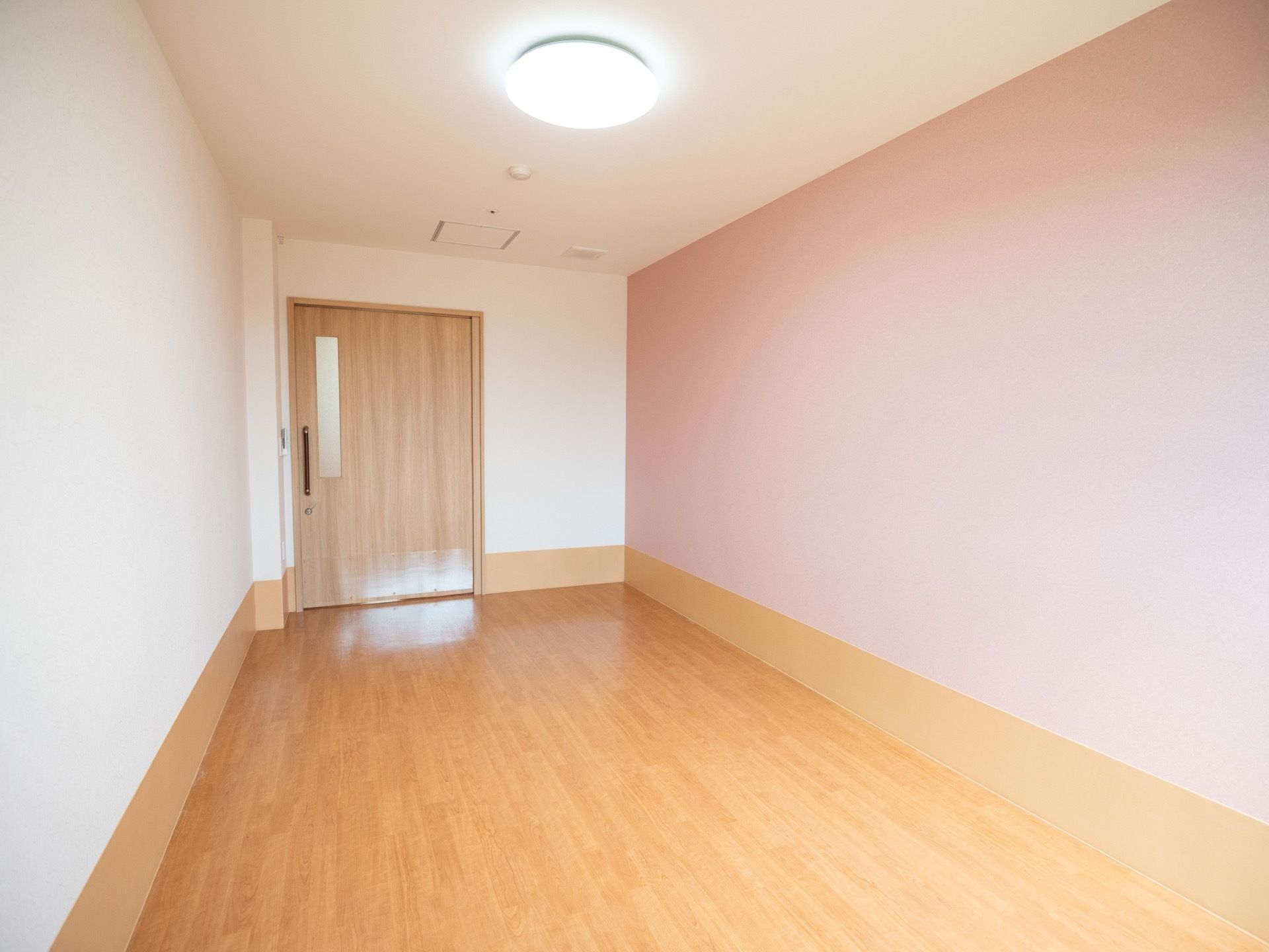 フローリングの床の広い個室で、ドアはスライド式になっている。天井に丸型の大きなライトがかかっている。