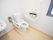 白い壁の個室トイレで、窓がある。壁にはトイレットペーパーホルダーとＬ字型の手すりがかかっている。