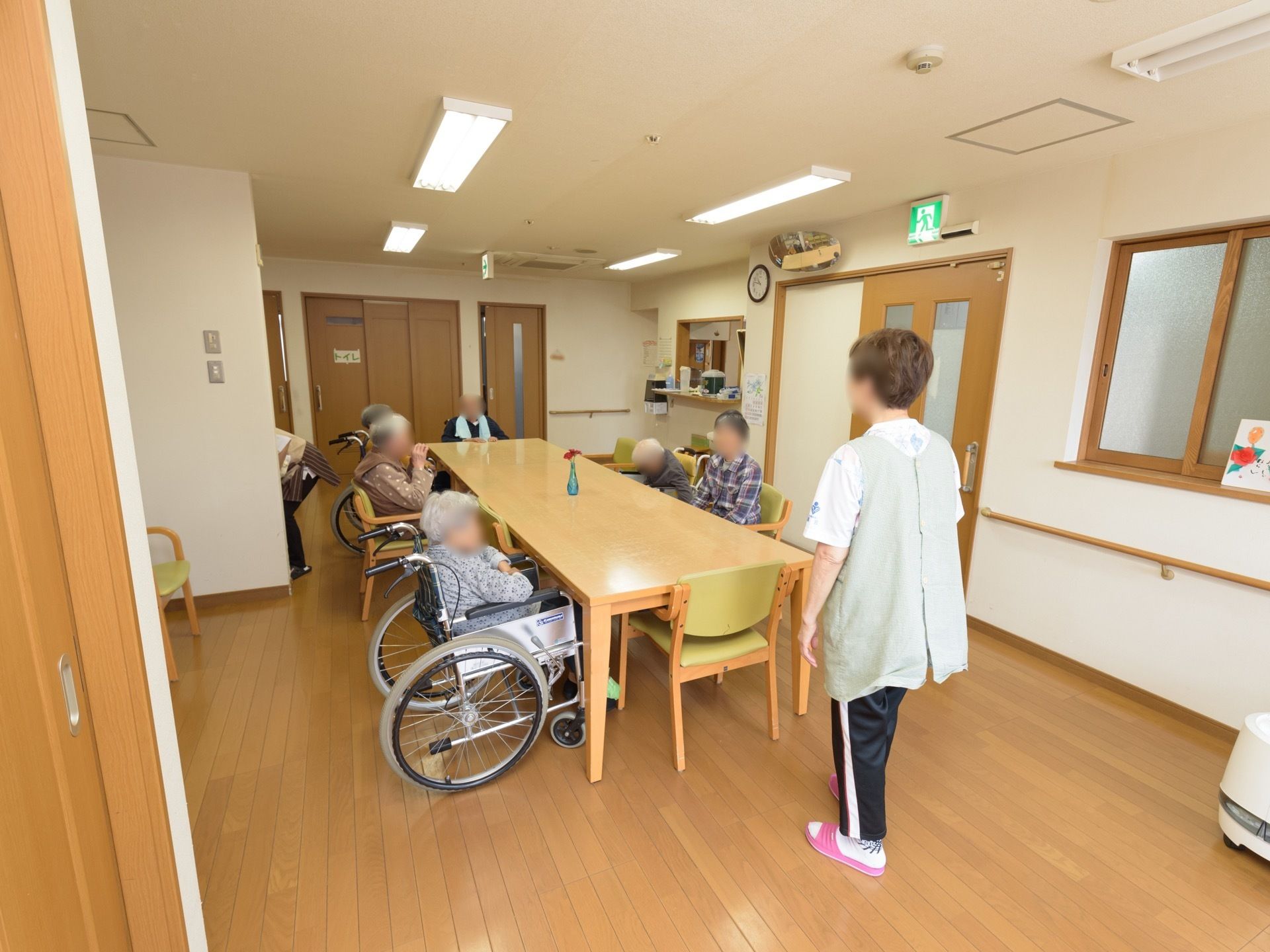 大きなダイニングテーブルが設置された共有スペース。車椅子をご利用の方がテーブルを囲み、会話を楽しんでいる。