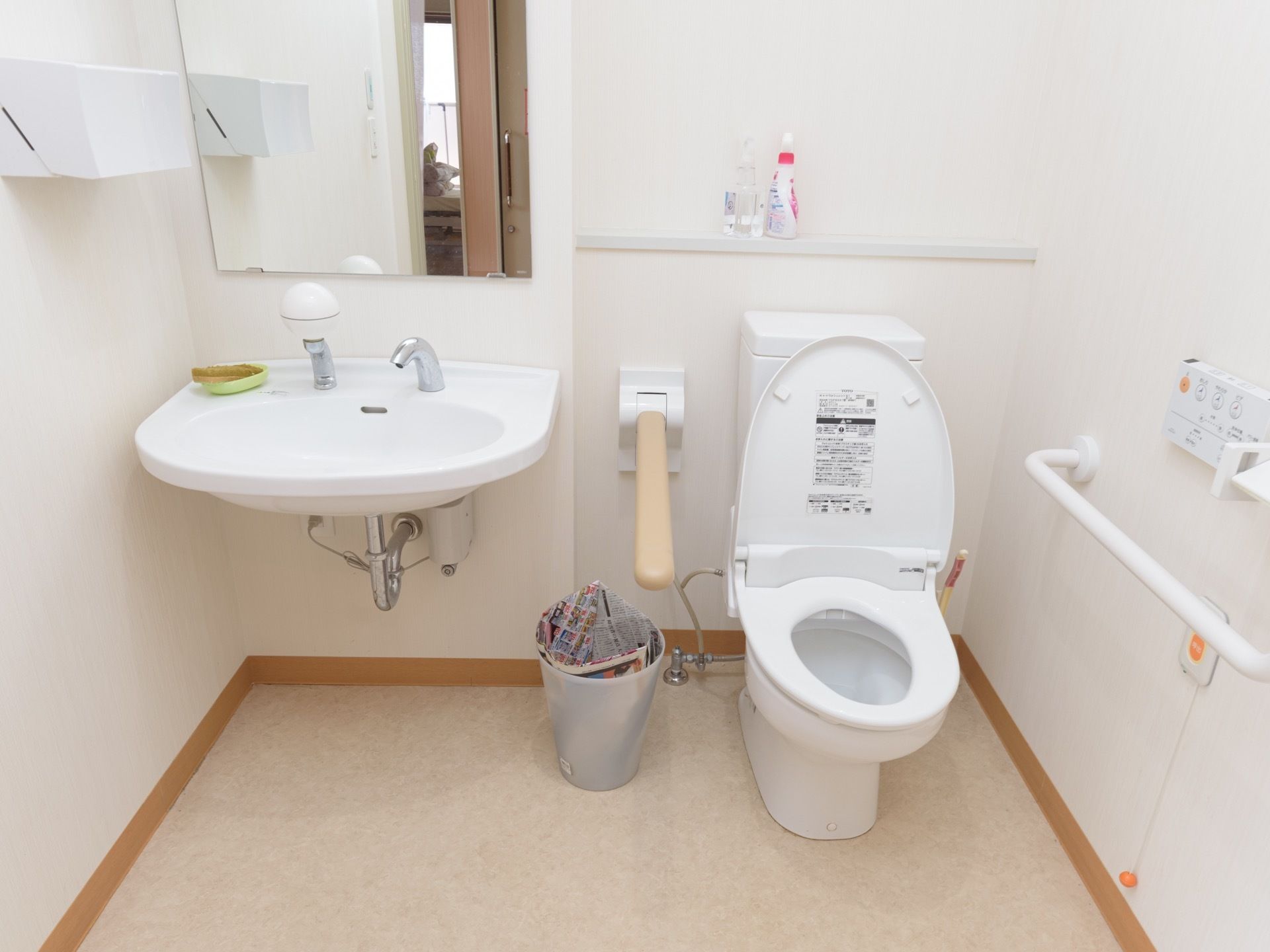 白で統一されたトイレである。右手に便座があり、左右に手すりが取りつけられている。洗面台にはスポンジが置かれている。