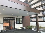 玄関先には大きな屋根が付き、自動ドアが設置されている。ドアの両サイドには鉢植えや傘立てなどがある。