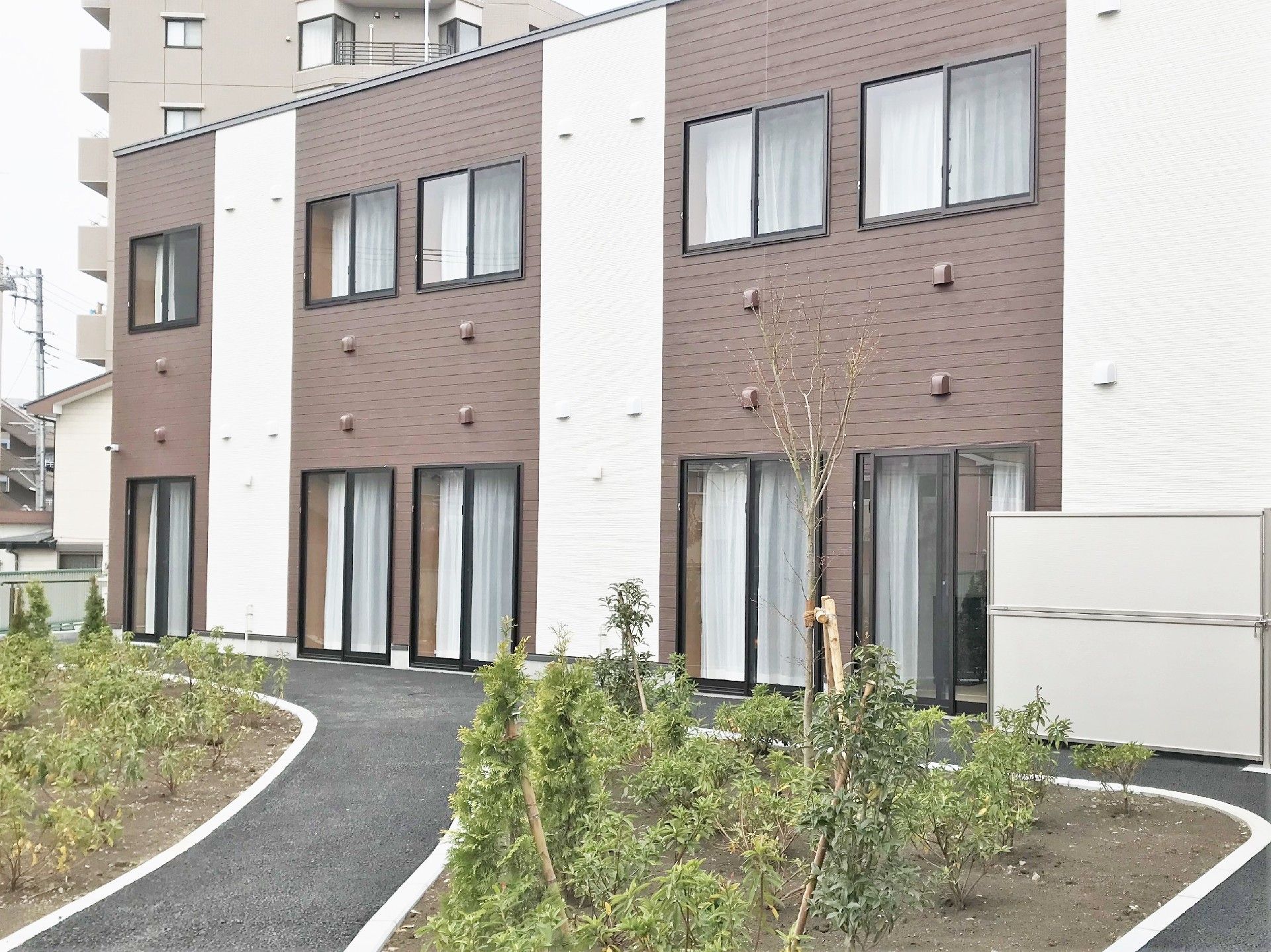 ２階建ての建物はブラウンと白で、敷地内にはたくさんの木が植えられている。