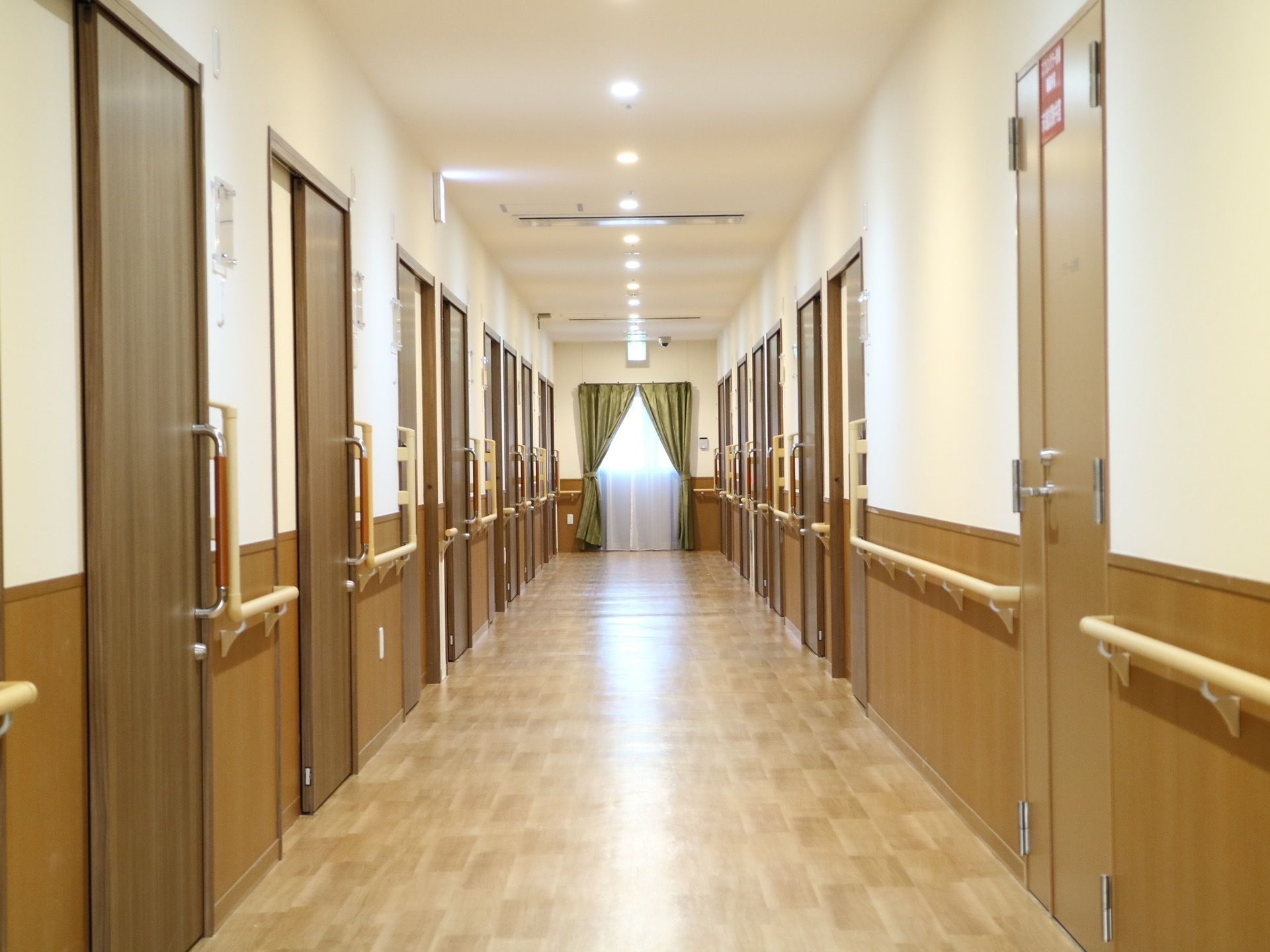 施設内の廊下はダウンライトで照らし、夜間も明るく通行がしやすい。安全のために壁には手すりが設置されている。