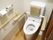 木目調の床に白い壁のトイレである。温水洗浄便座が設置され、可動式の手すりや背もたれなどが取り付けられている。
