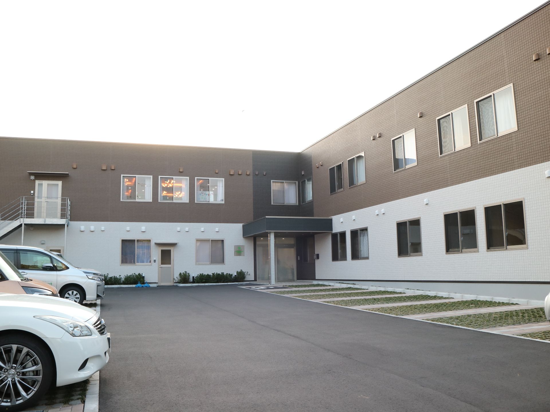 ブラウンと白の2階建ての建物は横に長く、建物の周辺には緑が多い。