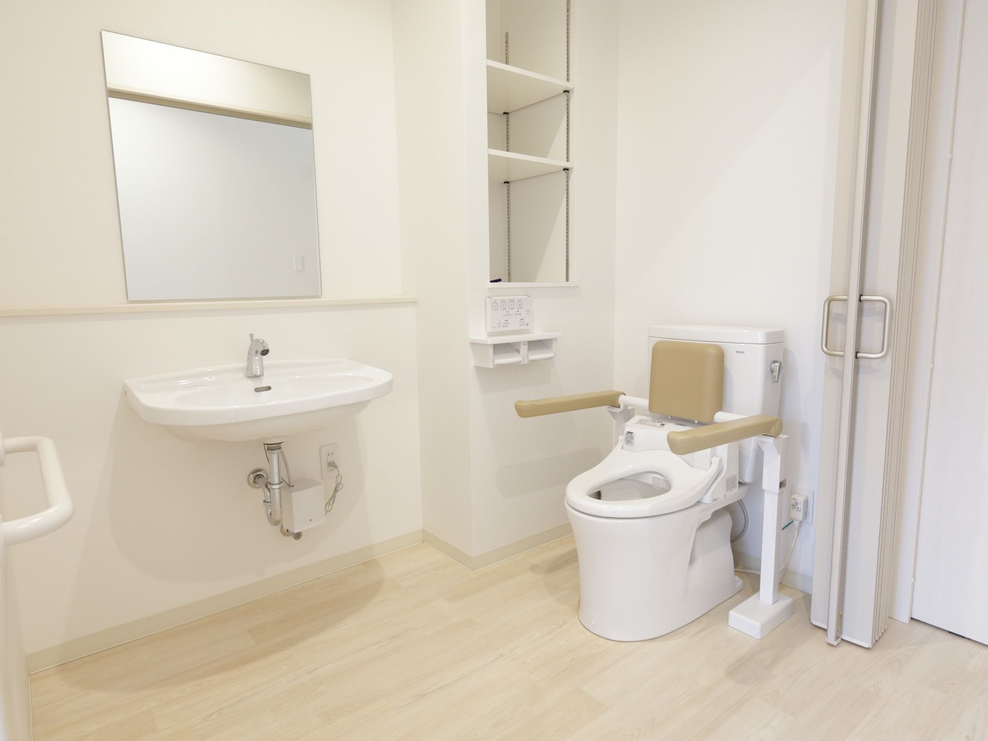 居室内のトイレスペースである。作り付けの収納棚や手洗いコーナー、タオル掛けなどがある。洋式便器に背もたれとひじ置きを設置している。