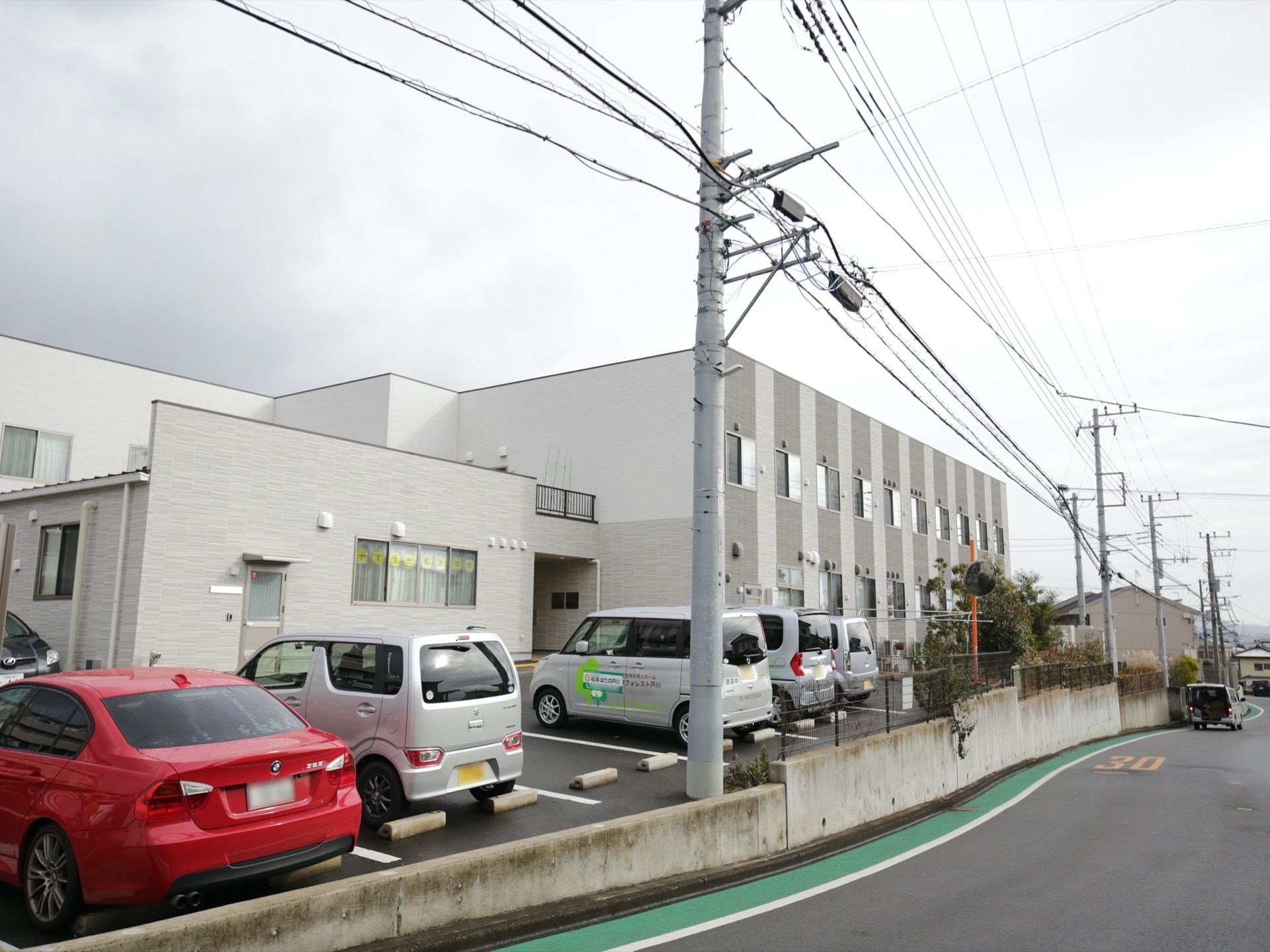 ２階建ての施設で、居室の窓は道路側に面しており、日当たりが良い。同じ敷地内に平置きの駐車スペースを設けている。