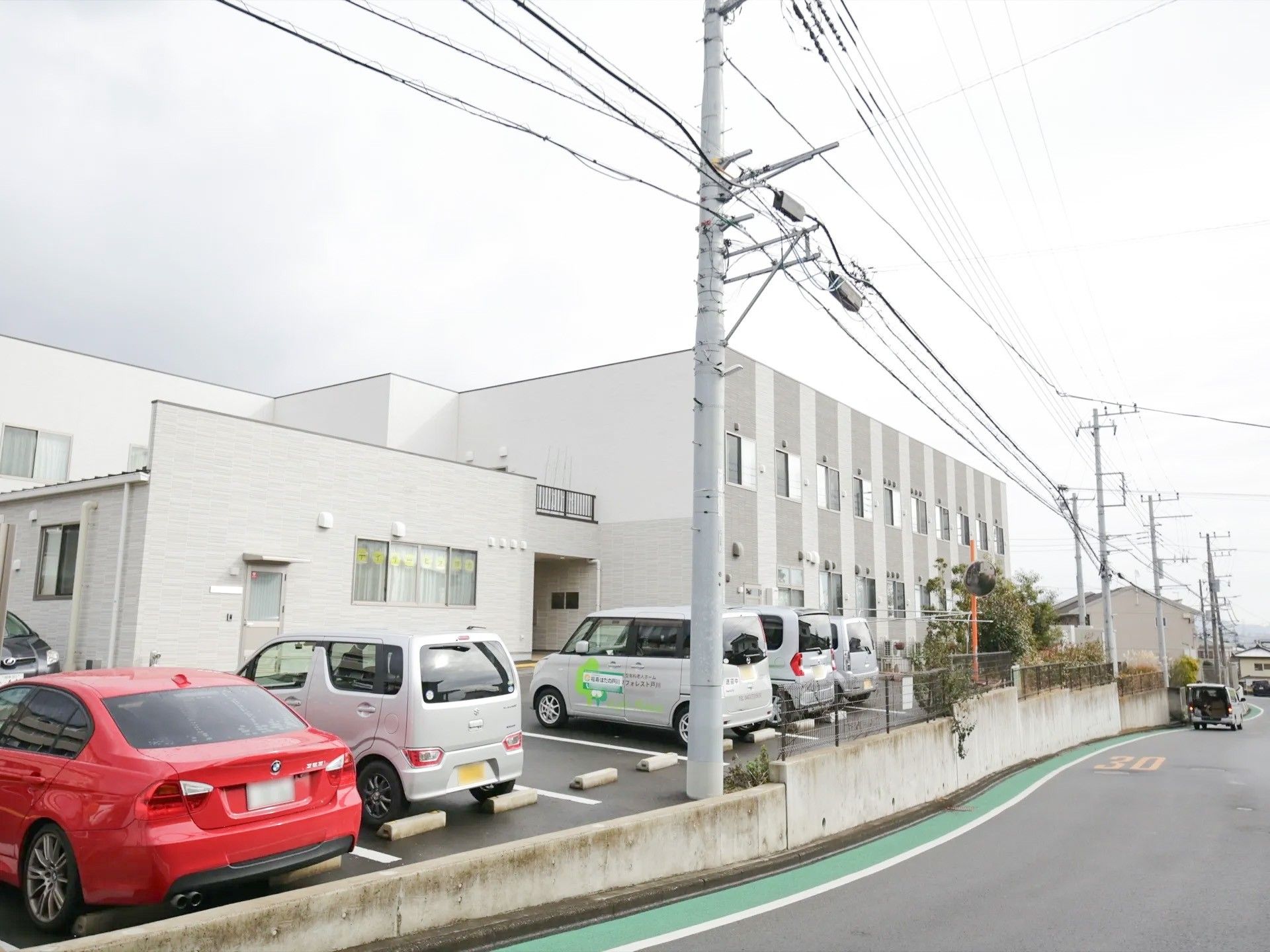２階建ての施設で、居室の窓は道路側に面しており、日当たりが良い。同じ敷地内に平置きの駐車スペースを設けている。