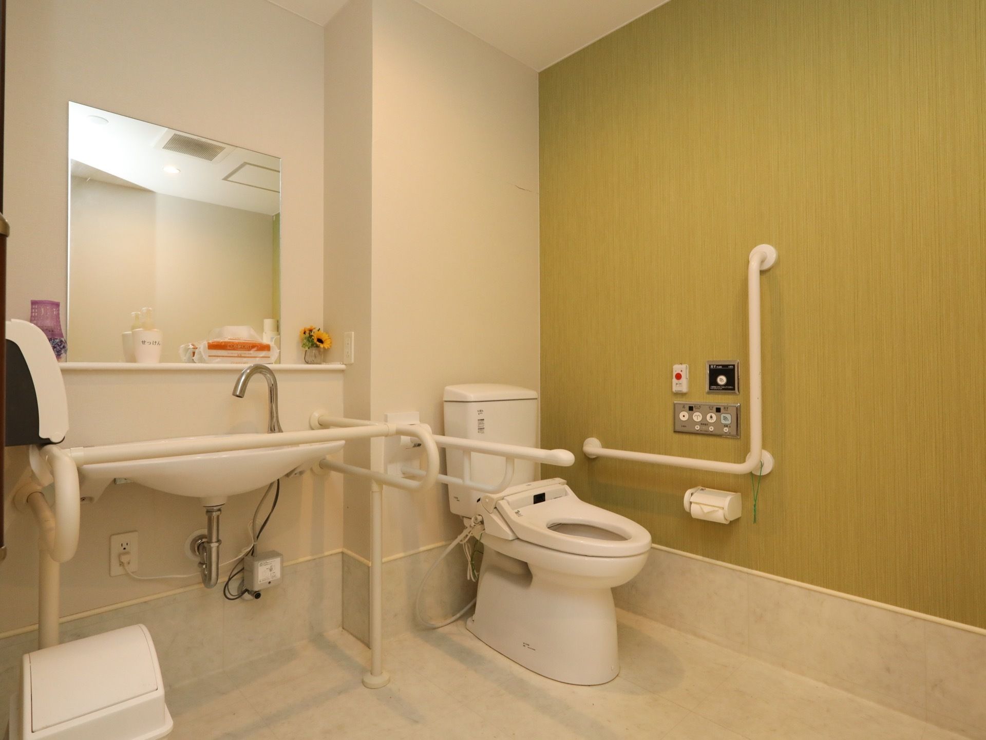 共用トイレは洗浄暖房機能つきの便座である。便座の近くに、シンクの周りに手すりがついた洗面台がある。