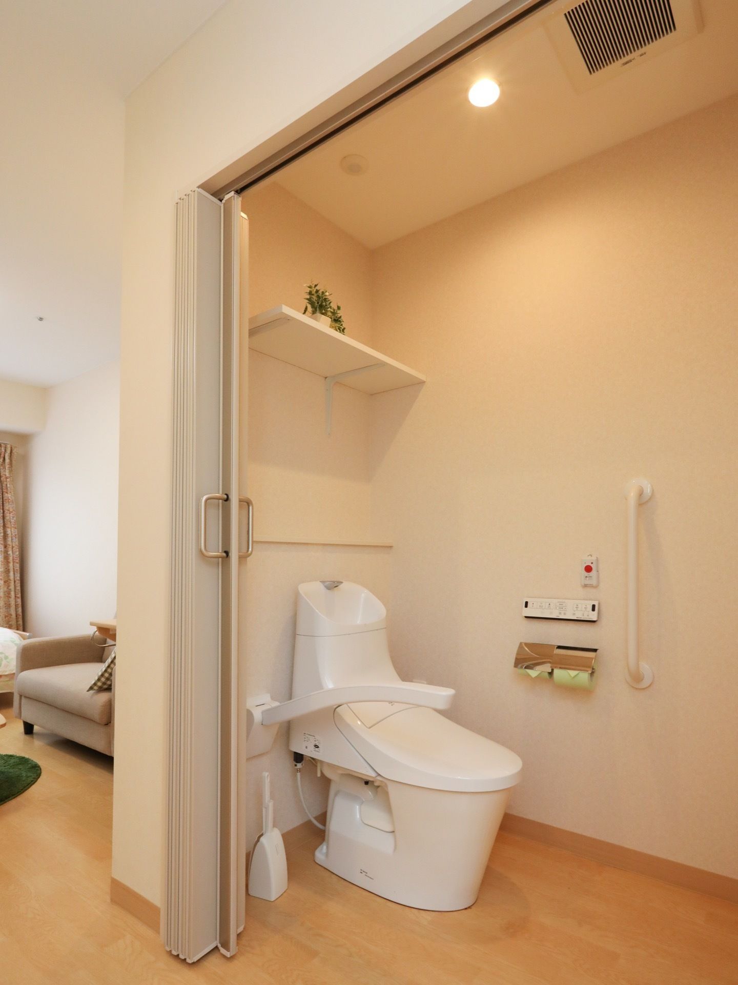 居室のトイレはじゃばらのカーテンの内側に設置されている。可動式の手すりが便座横に取り付けられている。