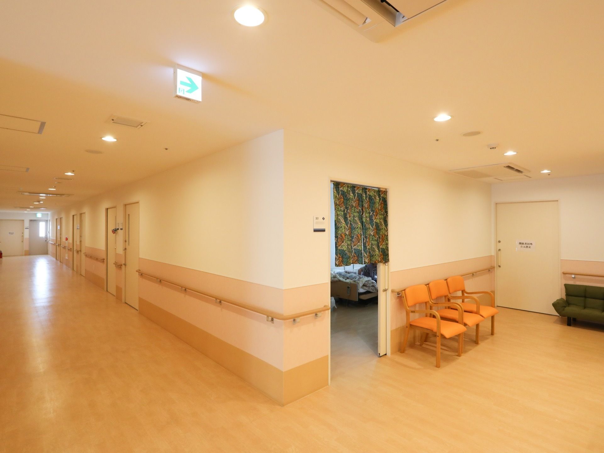 幅が広く見通しのよい廊下である。天井埋め込み式のエアコンがある。非常口の方向を示す矢印が天井についている。