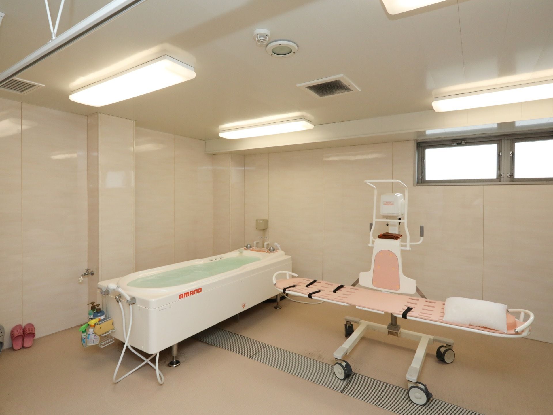 介護浴室がある。お湯を張った浴槽の横に可動式のピンク色のストレッチャーが置かれている。カーテンで仕切れるようになっている。