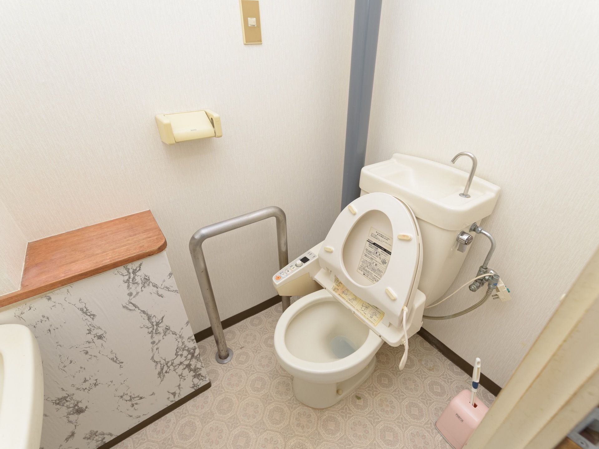 個室内に、洋式トイレと洗面台が設置されている。便器の脇に、身体を支えるためのシルバーの手すりが取りつけられている。
