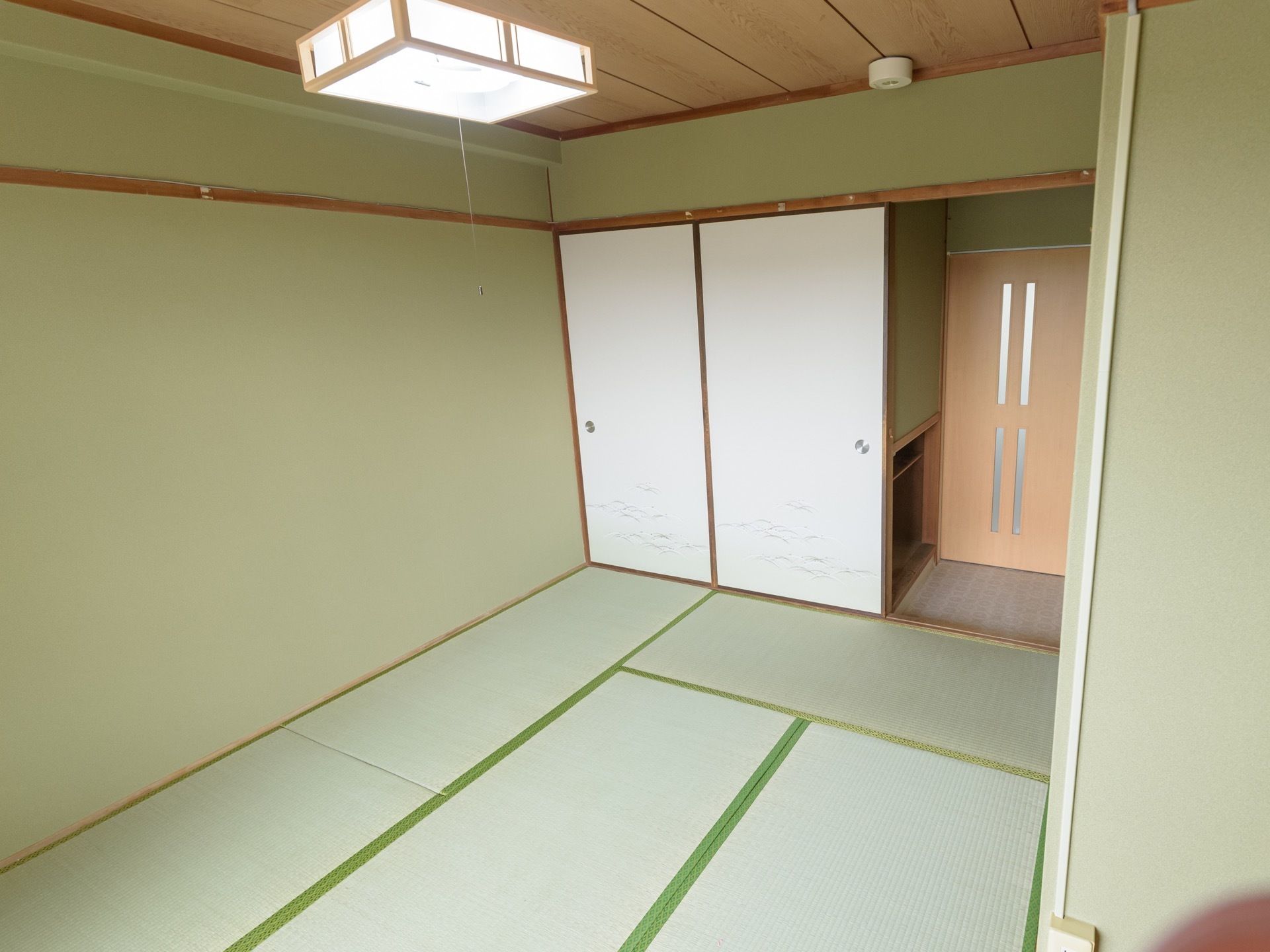 入口が淡いピンク色のドアの和室で、玄関部分は板の間になっている。押し入れや火災報知器が設置されている。