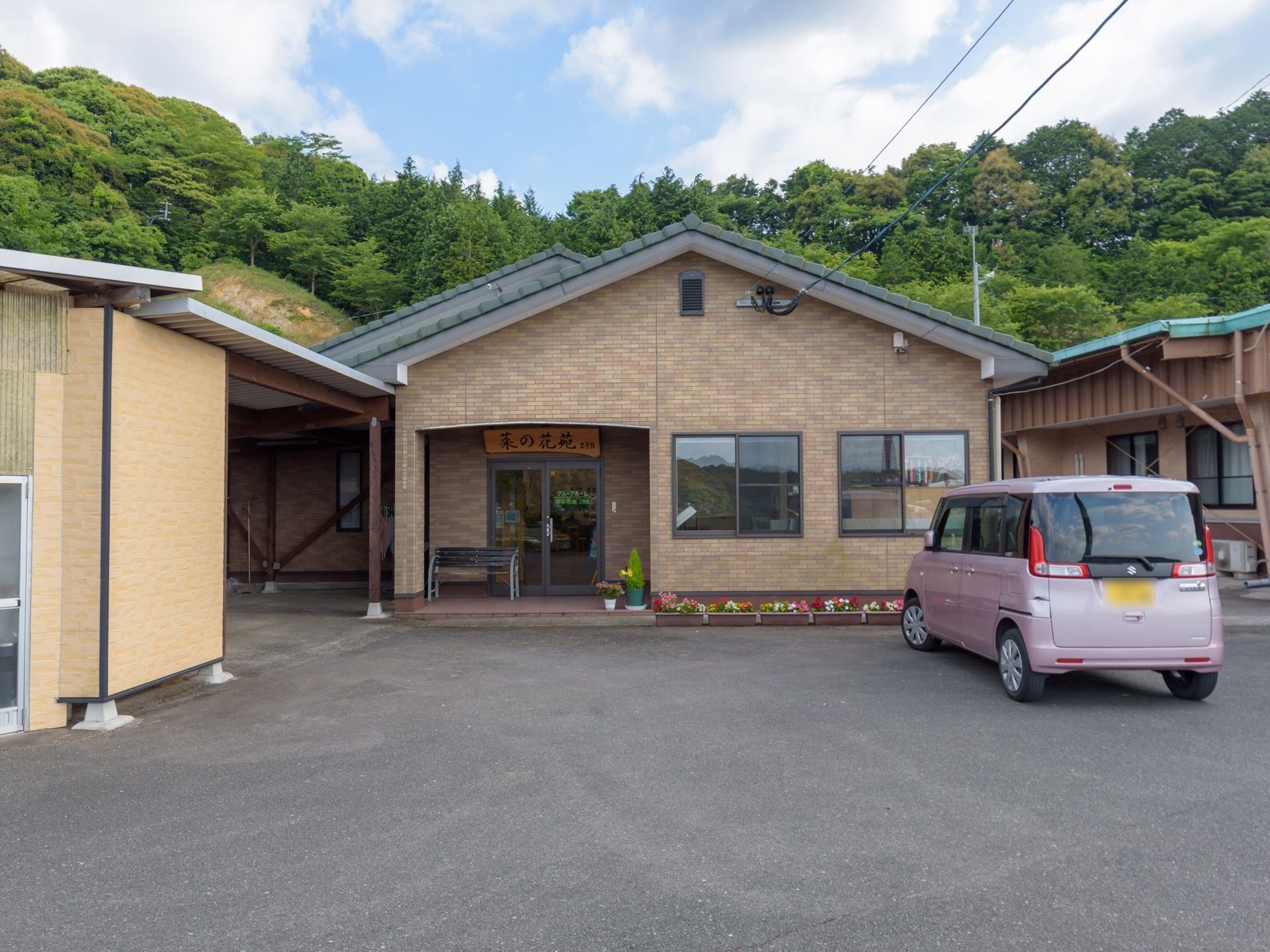 外壁がレンガ調の平屋建ての建物が建っている。アスファルトで整備された敷地に軽自動車が停められている。