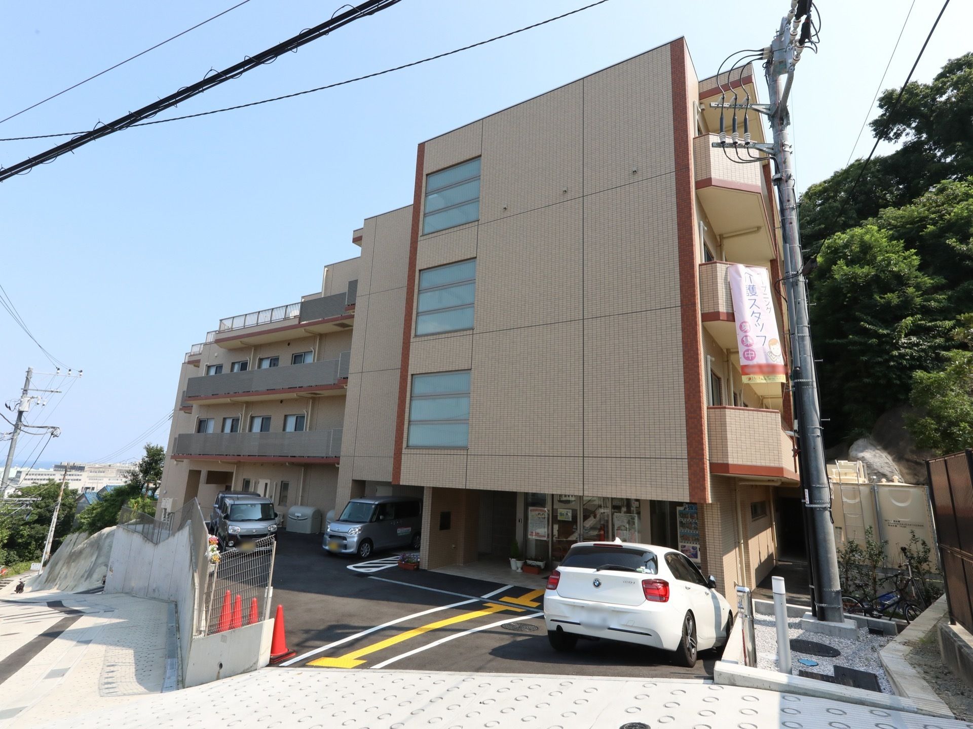 ブラウンを基調にした4階建ての建物で、駐車スペースも確保されている。１階部分には、飲料の自動販売機が設置してある。