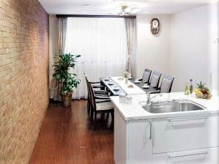 白いキッチンが付いた部屋には６人掛けのダイニングテーブルが置かれ、観葉植物も置かれている。