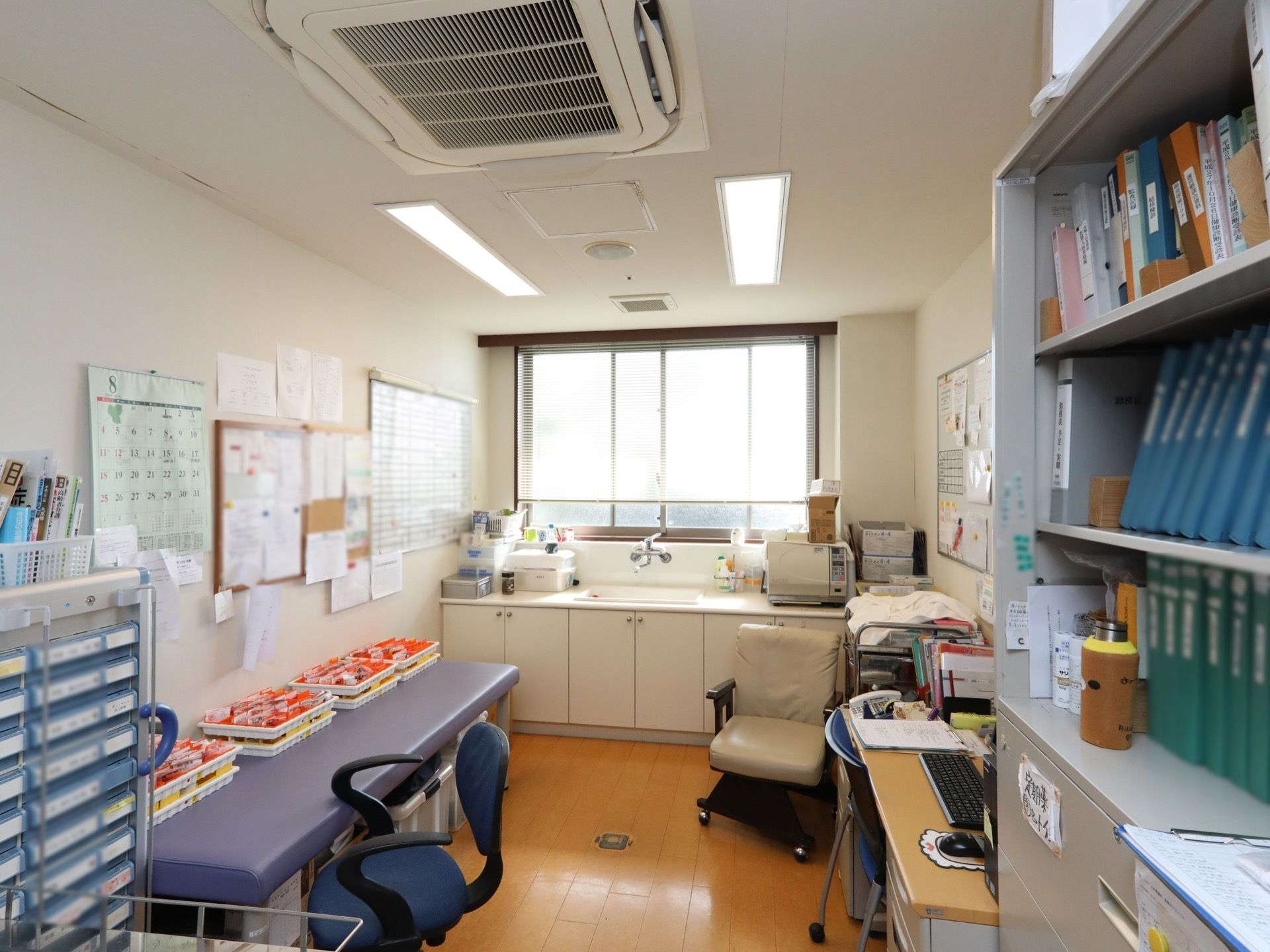 空調の付いたフローリングの部屋に、ファイルが並べられた棚やパソコン、デスク、洗面台などがある。