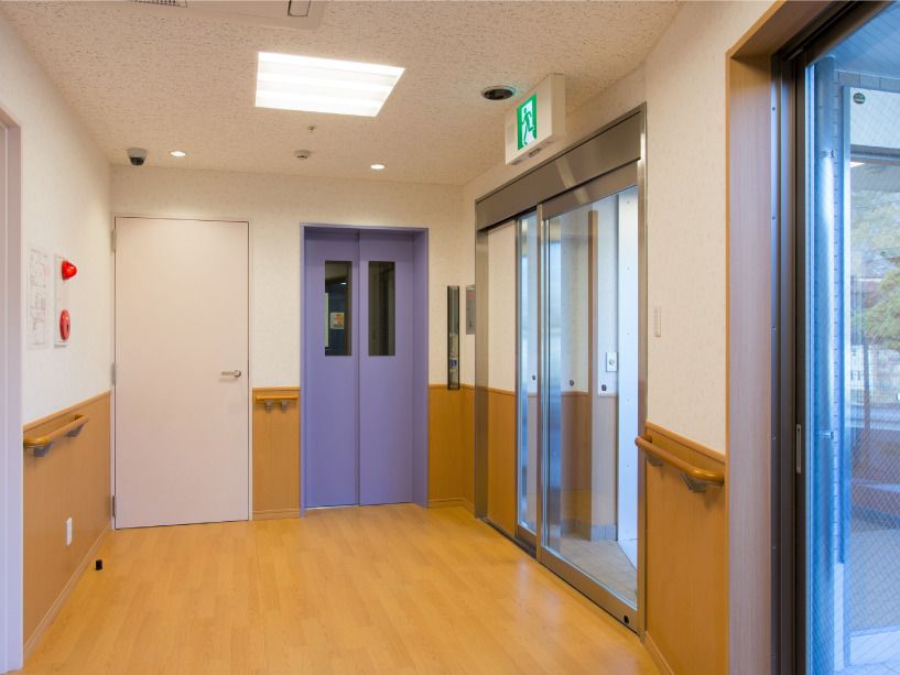 ブルーの扉がよく目立つエレベーター。すぐそばには防災設備も設置され、壁には木製の手すりも付いている。非常用の出口のサインもある。