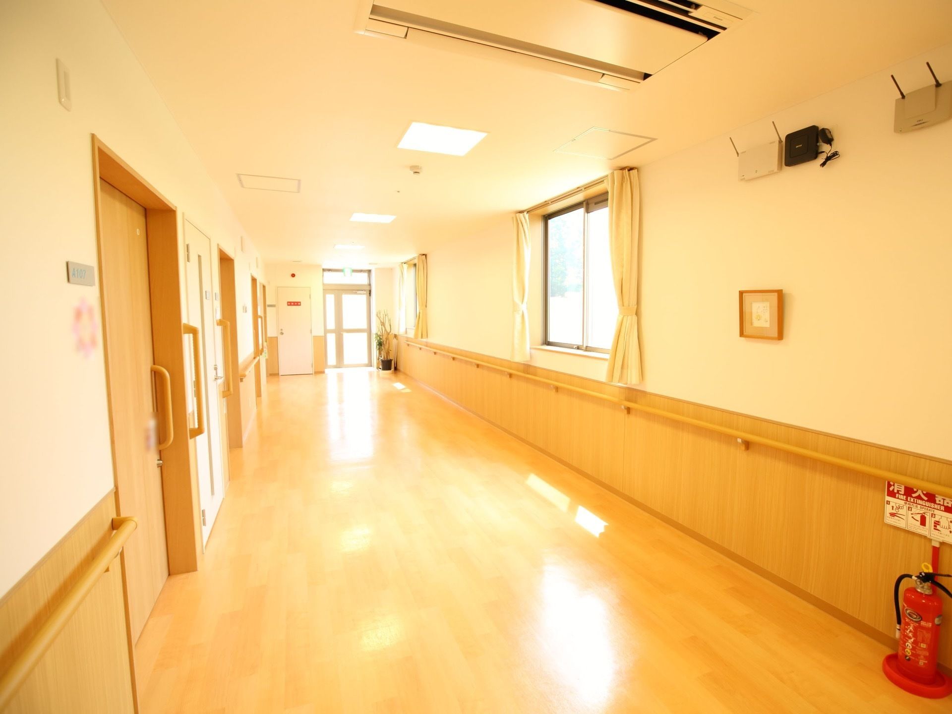 天井に空調の付いた広い廊下が伸びている。床はフローリングで、壁には大きな窓と手すりが設置されている。