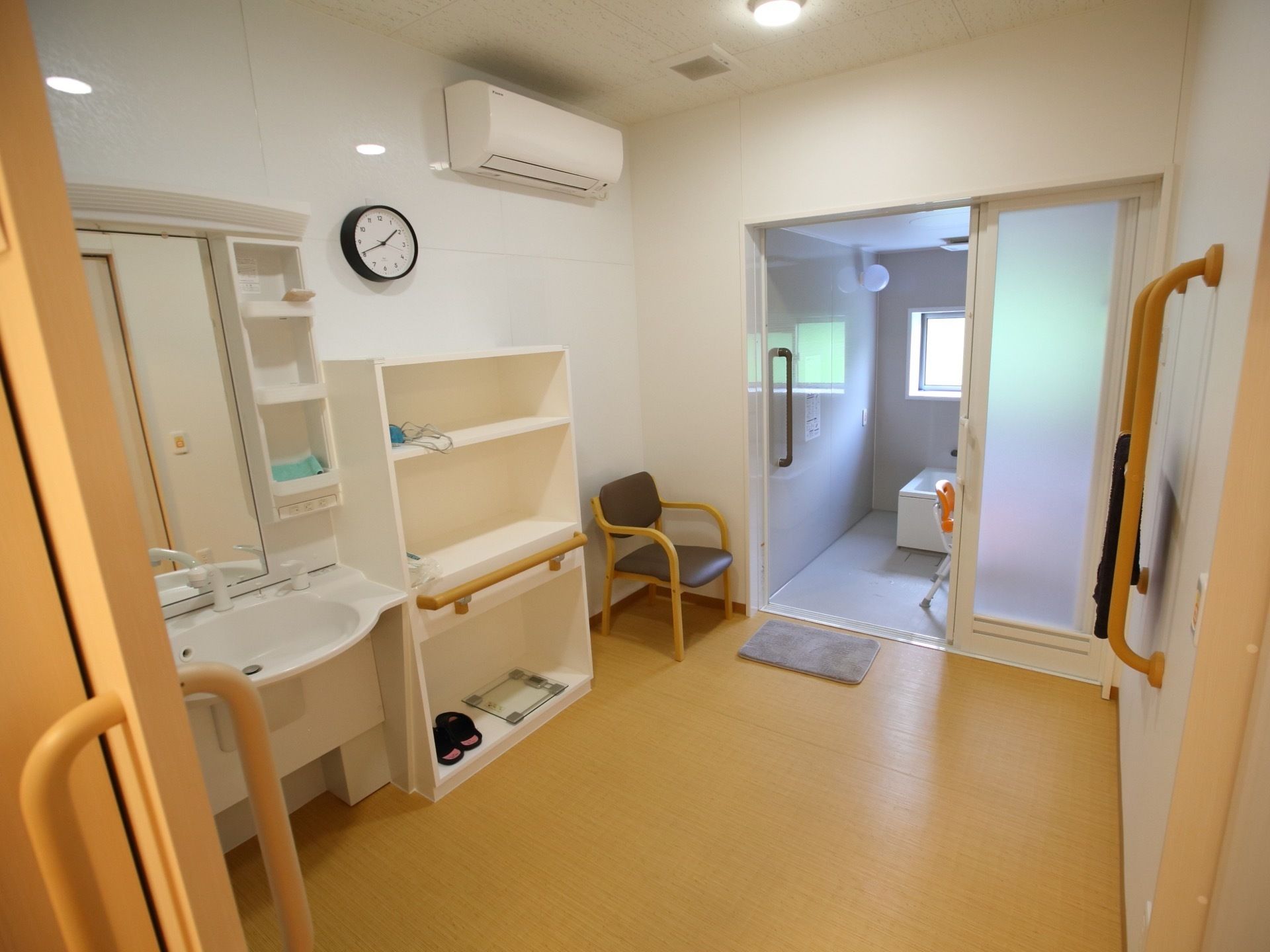 浴室の前に明るく広々とした脱衣所がある。洗面台や棚、着替え用の椅子があるほか、エアコンが設置されている。