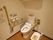 白い壁にフローリングのトイレがある。広々とした造りになっていて、便座の近くや壁には手すりが設置されている。