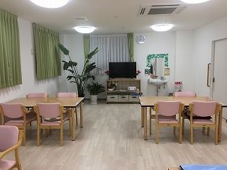 ピンクの椅子がセットされた木製のダイニングテーブルが複数置かれた食堂には観葉植物やテレビもある。