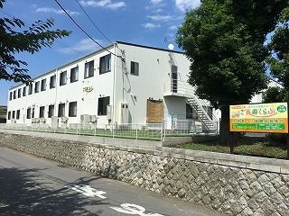 白を基調とした2階建ての建物は横に長く、敷地内には緑も多い。建物には屋外階段も付いている。