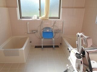 ピンクのタイルが貼られた浴室には一人用の浴槽が２つ設置され、右側の浴槽にはレールがあり、車いすタイプのリフトが設置されている。