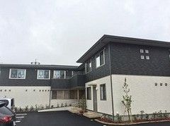 2階建ての建物は白と黒のツートーンで駐車場も完備。建物の周辺には緑が植えられている。
