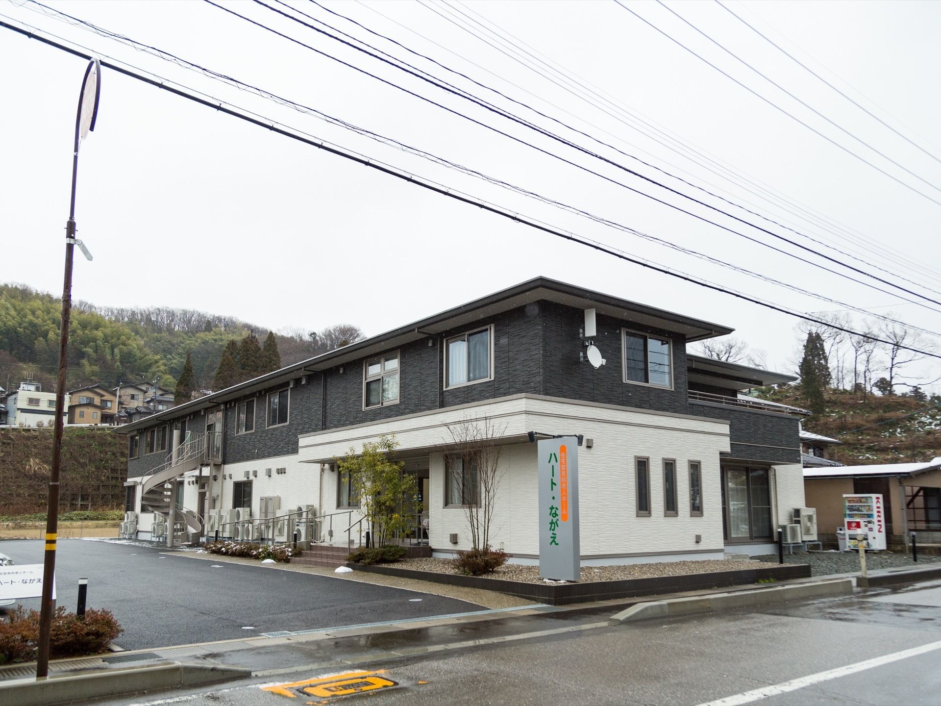 道路側から見ると、建物は奥に向かって細長い長方形をしている。外壁はグレーとホワイトのツートンカラーである。
