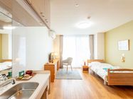 洗面所やベッド、デスクセットなどが付いたフローリングの部屋。天井にはスプリンクラーが設置されている。