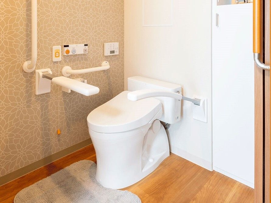 可動式の手すりやバーが付いたトイレには呼び出しボタンもあり、出入り口は幅の広い引き戸となっている。