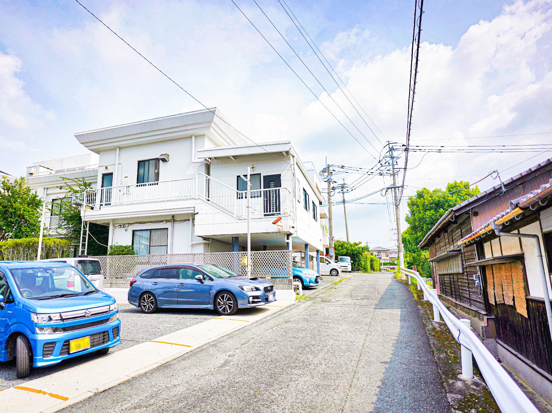 車が止まった駐車場に隣接した白い外観で２階建ての建物