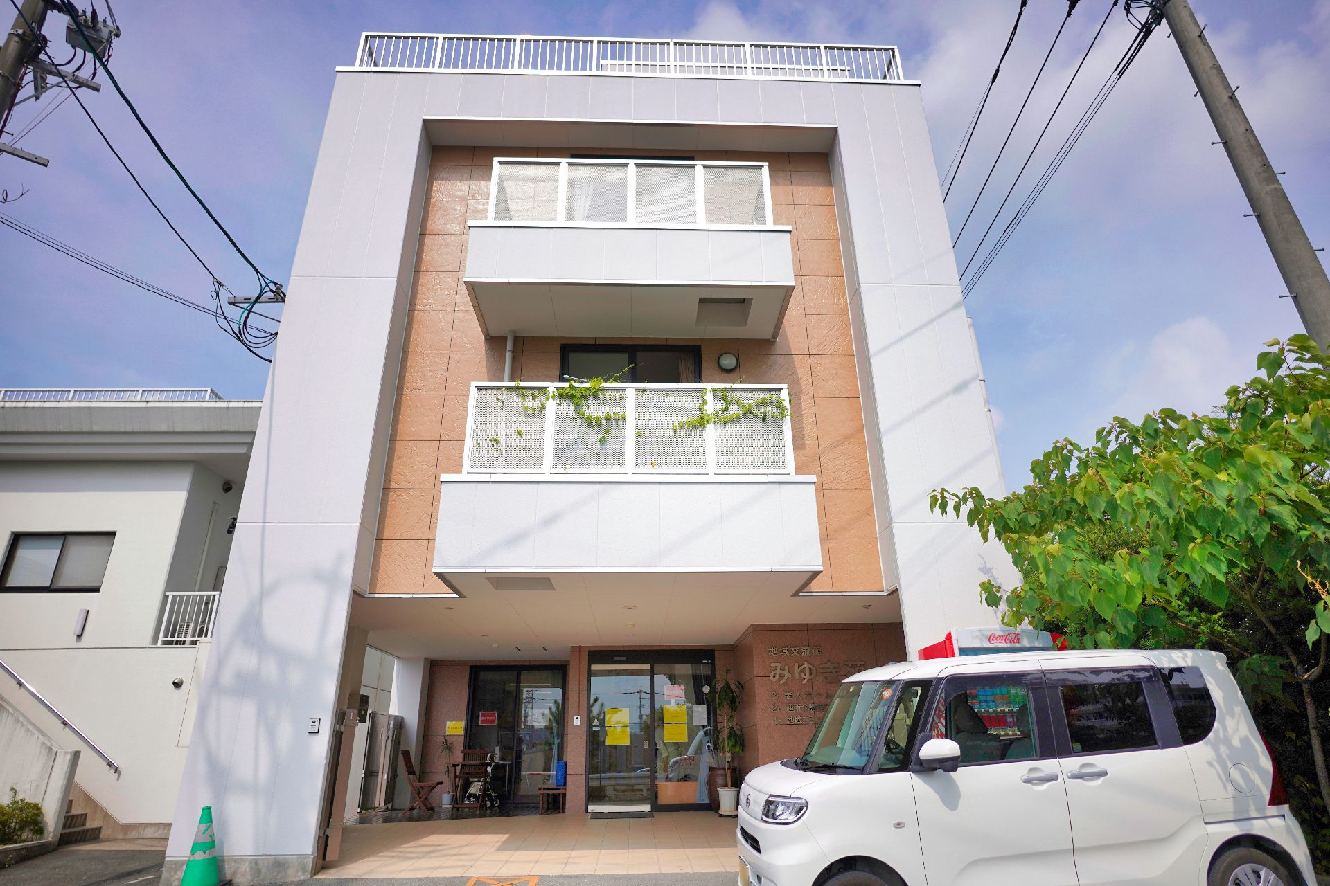 目の前に車が止まっている白とベージュの外観で３階建ての建物