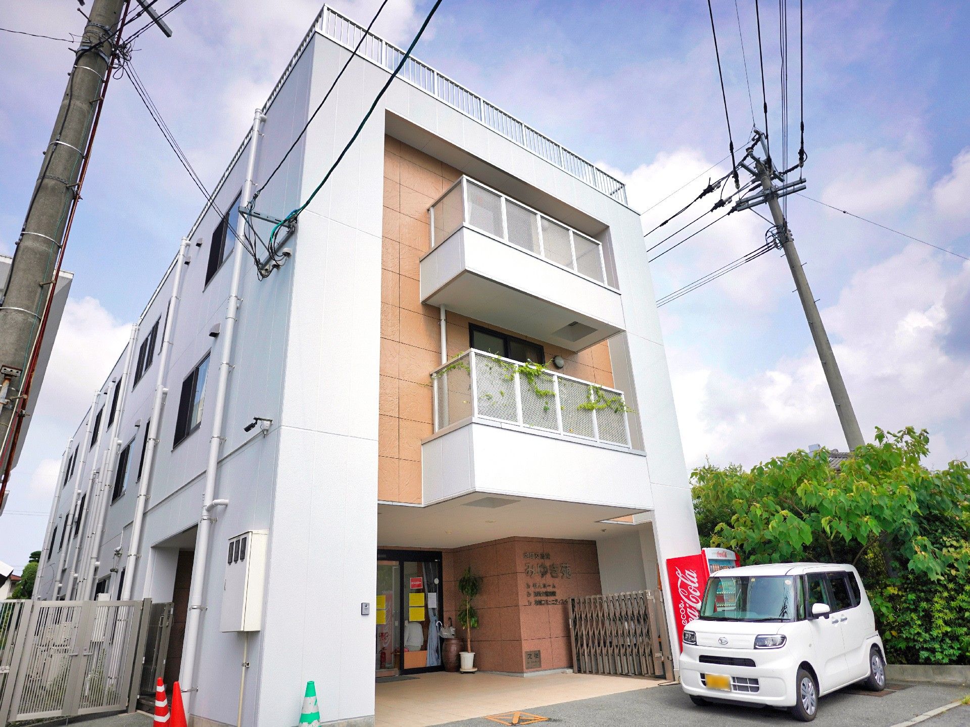 目の前に車が止まっている白とベージュの外観で３階建ての建物