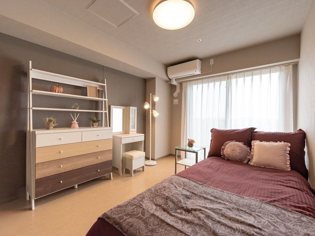 エアコンが付いた部屋には寝具付きのベッドが置かれ、大きな棚や鏡台があり、カーテン付きの大きな窓がある。