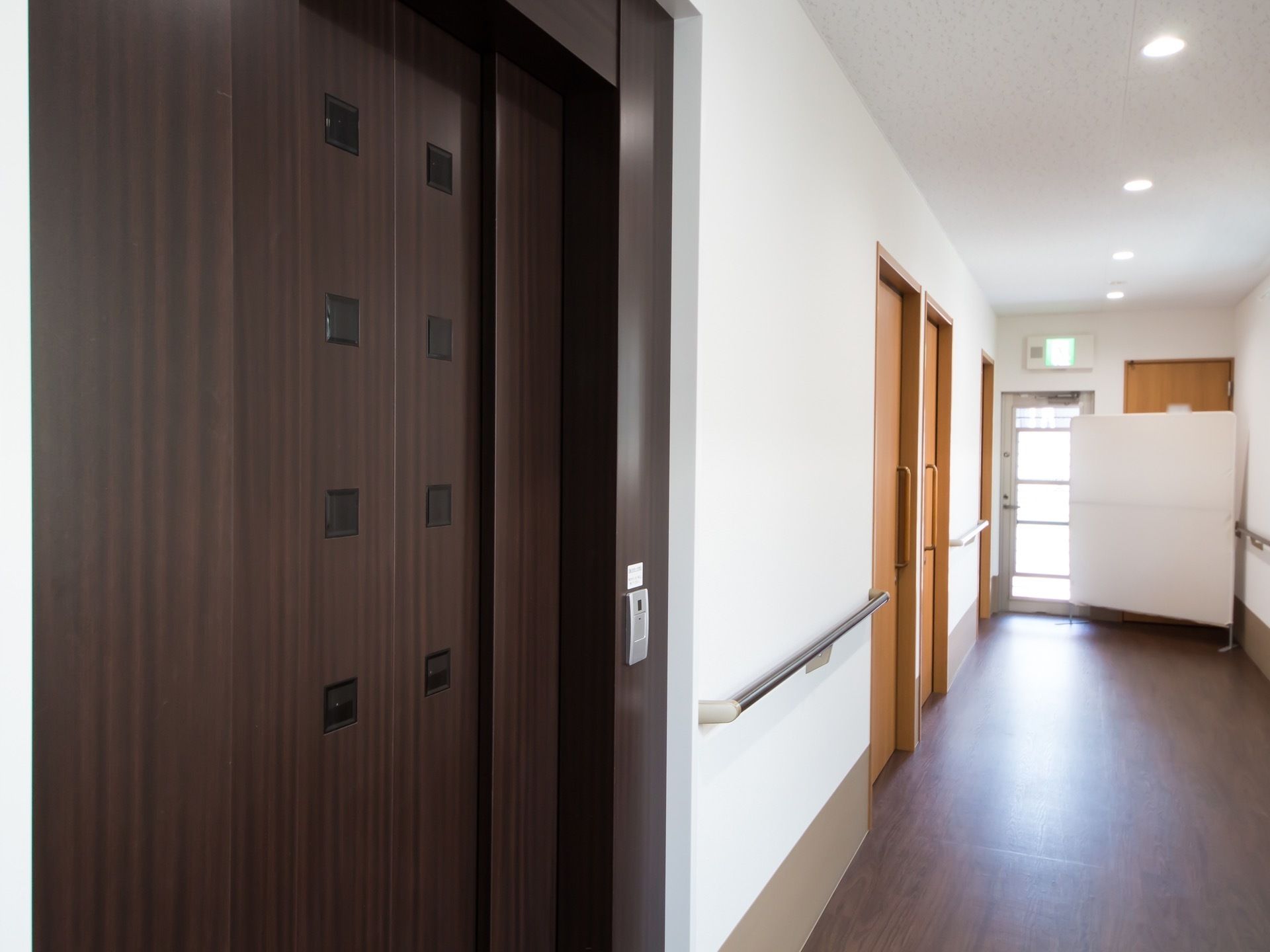 エレベーターホールの壁には手すりが取りつけられており、天井には丸い照明が設備されている。エレベーターのドアの横には、ボタンが設置されている。