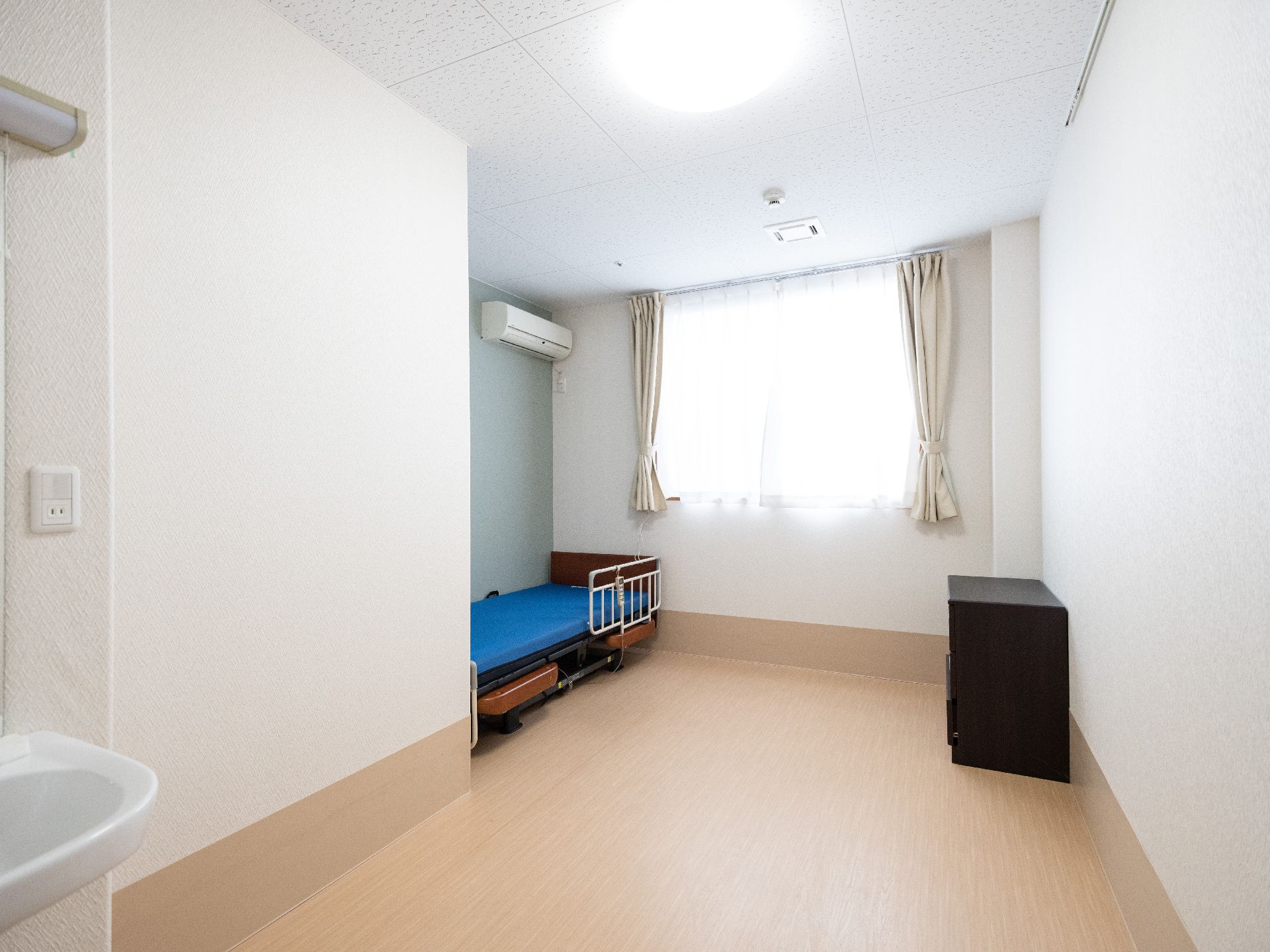 白い壁にアクセントクロスが貼られ、介護用ベッドが設置された居室